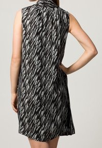 Schwarzes und graues ärmelloses Kleid mit abstraktem Muster, hohem Kragen und lockerem Schnitt, der über dem Knie endet.