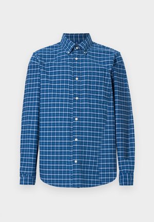 Chemise à manches longues à carreaux bleus avec un col boutonné, une poche avant et une texture subtile avec des nuances variées de bleu et de motifs à carreaux blancs.