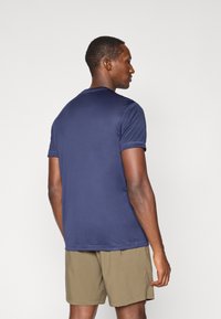 Navy blue short-sleeve athletic shirt with a round neckline, smooth fabric, and minimal seams, paired with light khaki shorts.