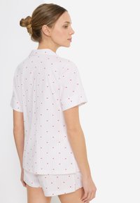 Σετ πυτζάμες με κοντά μανίκια από λευκό ύφασμα με κόκκινα σχέδια καρδιών και λεπτές ροζ ρίγες, δημιουργώντας ένα ελαφρύ και παιχνιδιάρικο σχέδιο.