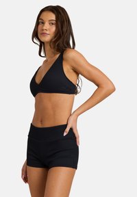 Μαύρο ριμπ τοπ μπικίνι με βαθύ ντεκολτέ και ταιριαστά σορτς ψηλόμεσα, με ομαλή υφή και μίνιμαλ σχεδιαστικές λεπτομέρειες.