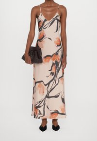 Robe maxi fleurie en pêche avec des lignes abstraites noires ; bretelles spaghetti ; tissu lisse. Associée à une pochette texturée sombre et des chaussures noires à bouts pointus.