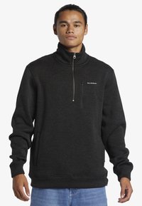 Čierny fleecový pulóver s vysokým golierom, zipsom na prednej strane a bočnými vreckami. Textúrovaná látka, voľný strih, jemný logotyp na hrudi.