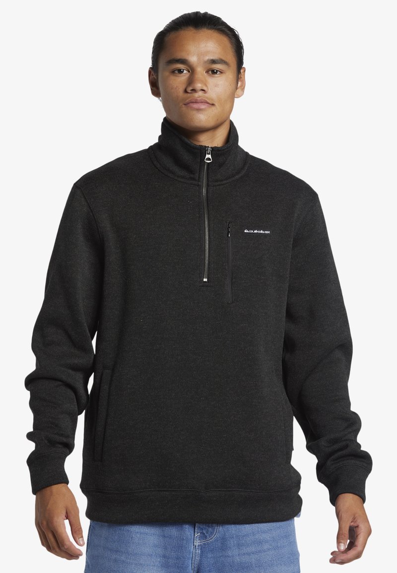 Čierny fleecový pulóver s vysokým golierom, zipsom na prednej strane a bočnými vreckami. Textúrovaná látka, voľný strih, jemný logotyp na hrudi.