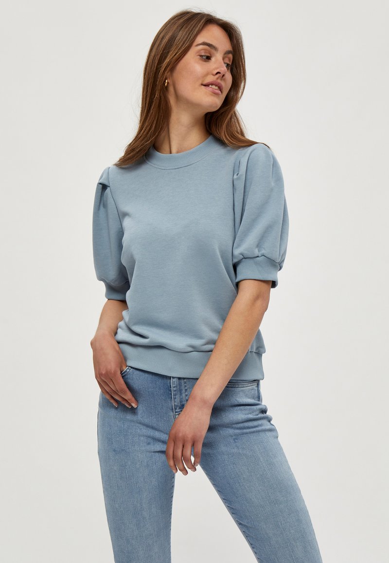 Ljusblå kortärmad sweatshirt med rund halsringning och puffärmar. Har ribbad mudd och fåll, tillverkad av mjukt tyg.