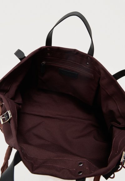 Sac fourre-tout en tissu marron foncé ouvert avec poignées noires, poche intérieure zippée et détail de boucle sur la sangle latérale.