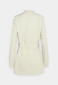 Blazer crème avec une coupe ajustée, manches longues, ceinture à l'arrière et col à revers cranté avec une surface texturée. Silhouette classique et taillée.