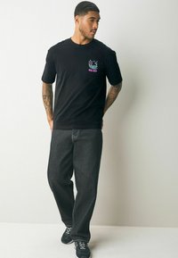 Tricou din bumbac negru, cu un design grafic colorat pe piept. Asortat cu blugi închiși la culoare și adidași negri.
