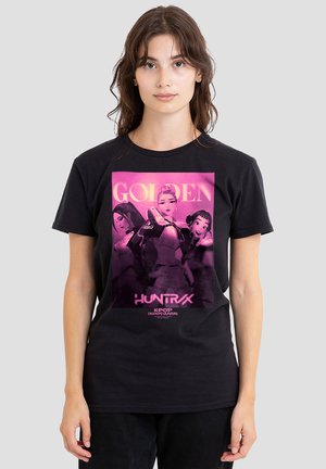 Young woman wearing black t-shirt featuring purple graphic of three animated female characters and text "Golden Huntrax K-pop Demon Hunters."