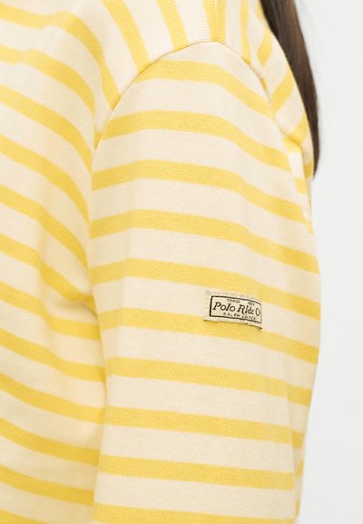 Μανίκι μακριάς μπλούζας με κίτρινες και λευκές ρίγες και λογότυπο Polo Ralph Lauren στο πάνω μέρος του μπράτσου.