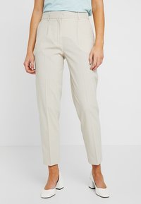 Beige op maat gemaakte broeken met een rechte pijp, geplooide voorkant en een gladde textuur, gecombineerd met witte blokhak schoenen.