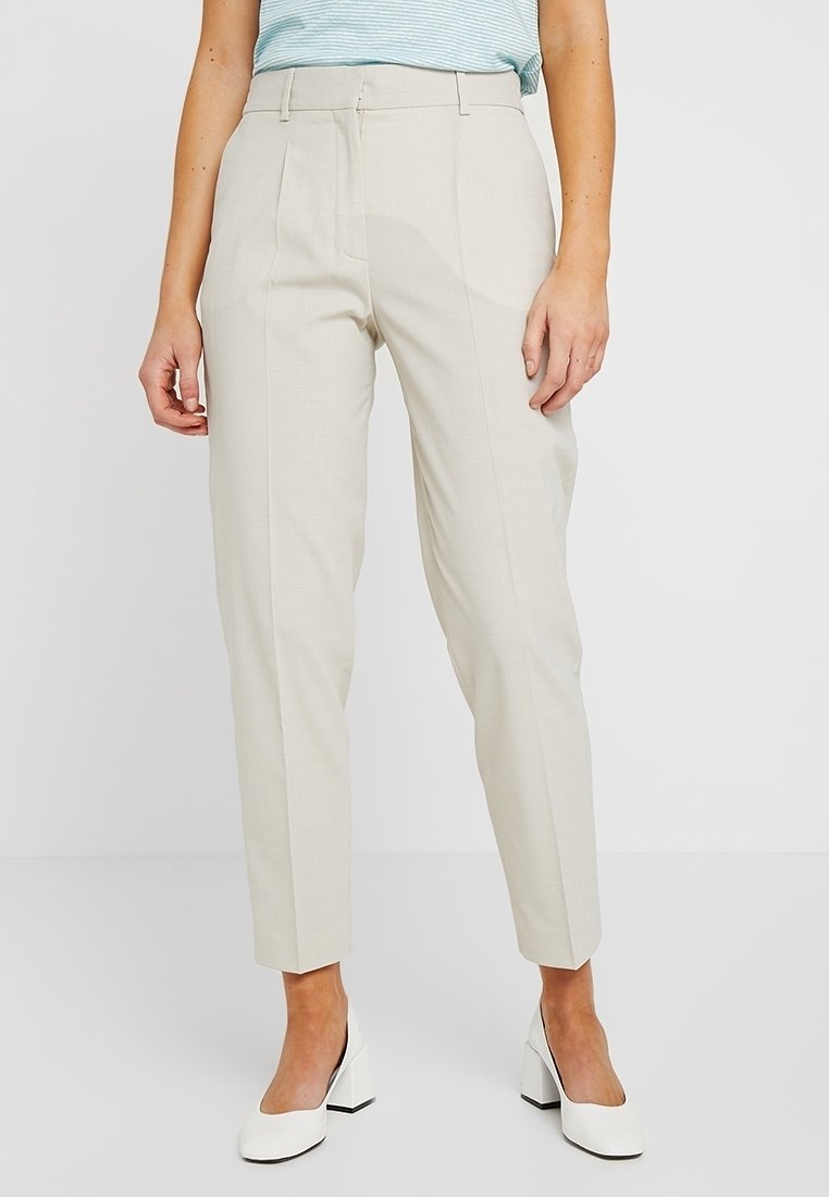 Beige op maat gemaakte broeken met een rechte pijp, geplooide voorkant en een gladde textuur, gecombineerd met witte blokhak schoenen.