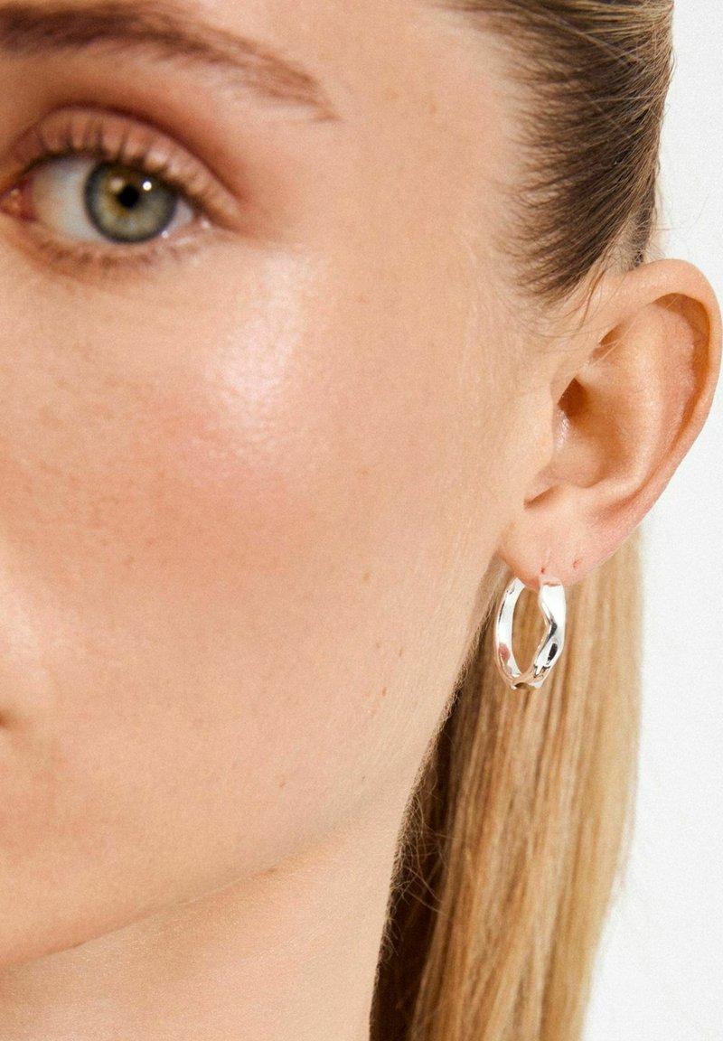 Silver hoop earrings featuring a twisted design, reflecting light with a polished finish. Designed to sit snugly against the ear.