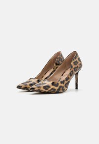 Talons hauts imprimés léopard avec un bout pointu, finition brillante et un talon aiguille élancé. L'intérieur présente une doublure de couleur chair.