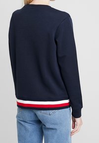 Felpa navy con collo rotondo, polsini a costine e un bordo con strisce rosse, bianche e blu. Tessuto morbido con un taglio informale.