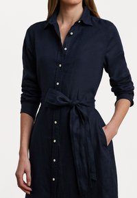 Navy blue linen dress with a button-front, long sleeves, a belted waist, and pockets. Soft texture with a classic collar design.