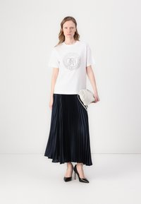 Hvit kortermet t-skjorte med sirkelgrafikk, parret med en marineblå plisserte skjørt, svarte høye hæler og en lysfarget clutch-veske.