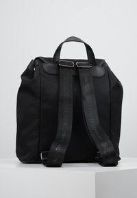 Black nylon backpack with leather accents, two adjustable straps featuring logo, top handle, and minimalist shape.