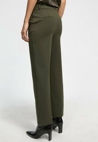 Pantalones de pierna ancha en verde oliva con cintura alta y detalle de bolsillo trasero, combinados con botas de tacón negro de punta afilada.