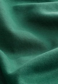 Tela de color verde azulado, suave y doblada, con una textura de punto fina visible y sombras sutiles que destacan los contornos y el patrón de tejido del material suave.
