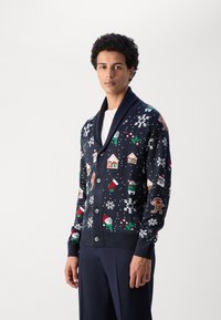 Sötétkék kardigán karácsonyi motívumokkal díszítve, mint a hópelyhek, mézeskalács emberkék és házikók; stólakolár és gombok találhatók rajta.