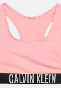 Ανοιχτό ροζ αθλητικό σουτιέν με σχεδίαση racerback και φαρδιά μαύρη ελαστική ταινία στο κάτω μέρος με λευκό κείμενο "CALVIN KLEIN".