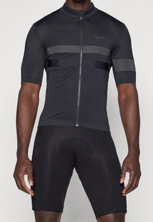 Man wearing a fitted black cycling jersey with horizontal stripes and matching black padded cycling shorts against a plain background.