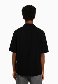 Black short-sleeve collared shirt with a straight cut, featuring a smooth texture and simple design, viewed from the back.