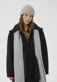 Black wool coat with large collar, buttons, and a tie belt. Accompanied by a light grey knit scarf and matching ribbed beanie. Soft textures.