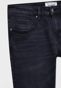 Jeans de mezclilla azul oscuro, con un diseño de cinco bolsillos, costuras visibles y una etiqueta de marca en la cinturilla.