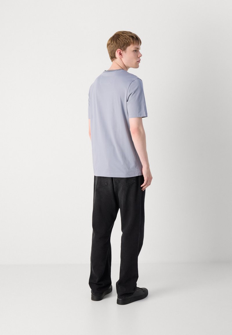 T-shirt grigio chiaro a maniche corte con una vestibilità rilassata, abbinato a pantaloni neri larghi. Design semplice, texture liscia, senza motivi visibili.