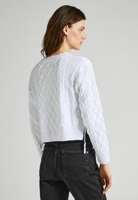 Pullover bianco lavorato a maglia con motivi a treccia e polsini a costine, dal design corto e con dettagli testurizzati sul tessuto.