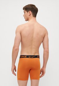 Boxers ajustados laranja da Nike com uma faixa elástica preta apresentando o logótipo da Nike. Design ajustado e tecido macio. Vista traseira mostrada.
