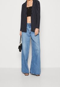 Námořnický blejzr s pruhy, černý krátký top, široké světle modré džíny z texturované látky, volný střih, doplněno černou kabelkou a sandály.