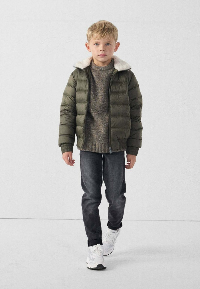 Giacca a vento verde con colletto foderato in pelliccia, maglione grigio testurizzato, jeans scuri e sneakers bianche, indossata da un bambino.