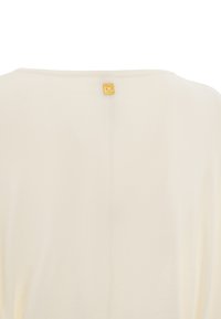 Haut crème avec une coupe décontractée, présentant une texture délicate et une petite étiquette dorée à l'arrière du cou. Design simple et minimaliste.