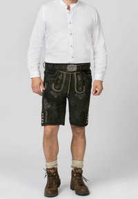 Shorts en cuir noir avec broderies décoratives, associés à une chemise blanche à boutons et des bottes en cuir marron à lacets. Chaussettes en laine visibles.