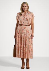 Blomster maxi kjole i myk rosa stoff, med volanger på ermene, knytning ved halsen, lagdelt skjørt og et brunt belte. Brune åpen-tå hæler.