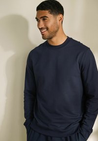 Marineblauwe crewneck sweatshirt van een zachte, elastische stof met lange mouwen en geribbelde boorden. Aansluitend ontwerp met een subtiele glans.