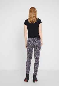 Jeans ajustados con un patrón de rayas de cebra en negro y gris, con una cinturilla alta y un bolsillo trasero, combinados con una blusa negra ajustada y tacones negros.