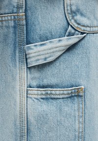 Υφασμα από ανοιχτό μπλε ντένιμ με τρεις ορατές τσέπες και αντίθετη πορτοκαλί ραφή, που δείχνει υφή και στρωματοποιημένο σχεδιασμό τσέπης.