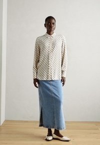 Button-up shirt with a cream and black diamond pattern, paired with a denim maxi skirt featuring a front slit and white slip-on shoes.