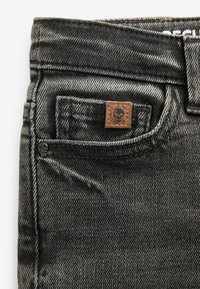 Jeans in denim nero con una trama strutturata, design a cinque tasche e una toppa in pelle marrone con un logo a teschio sulla tasca posteriore.