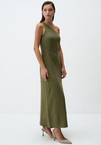 Olivgrünes Ein-Schulter-Kleid mit tailliertem Oberteil und fließendem Rock. Glatte Textur mit seitlichen Nähten, kombiniert mit strukturierten beigen High Heels.