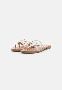 Hvite flate sandaler med flere kryssende stropper laget av syntetisk materiale, med en glatt, brun kunstskinn innersåle.