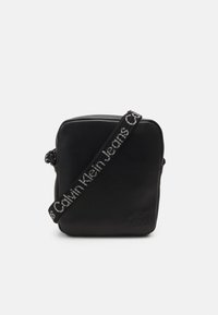 Borsa a tracolla in pelle nera con forma quadrata. Presenta una finitura testurizzata e una tracolla regolabile con logo "Calvin Klein Jeans".