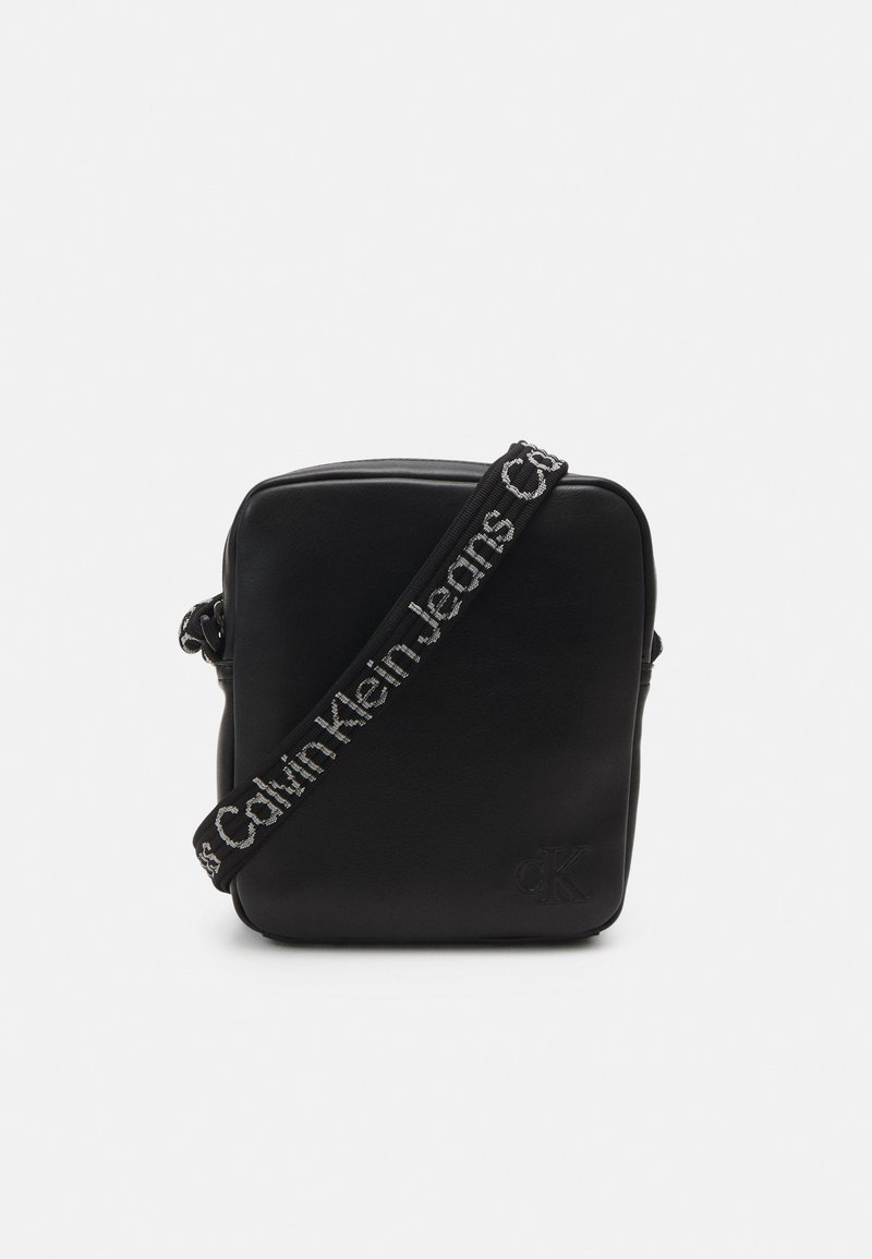 Borsa a tracolla in pelle nera con forma quadrata. Presenta una finitura testurizzata e una tracolla regolabile con logo "Calvin Klein Jeans".