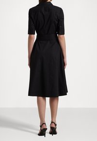 Svart skjortklänning med korta ärmar, figursydd midja och utsvängd kjol. Tillverkad av bomullsblandning, med klassisk krage och detalj med bakveck.