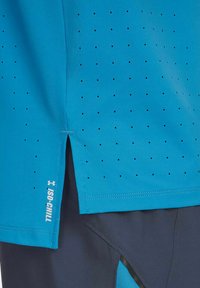 Camiseta deportiva turquesa hecha de tejido transpirable, con pequeñas perforaciones negras, abertura lateral y la marca "ISO-CHILL" en el dobladillo.