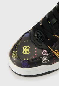 Sapatilha sintética preta com padrões de logo multicoloridos, superfície texturizada, atacadores pretos e sola de borracha branca. Apresenta um design de bico redondo.